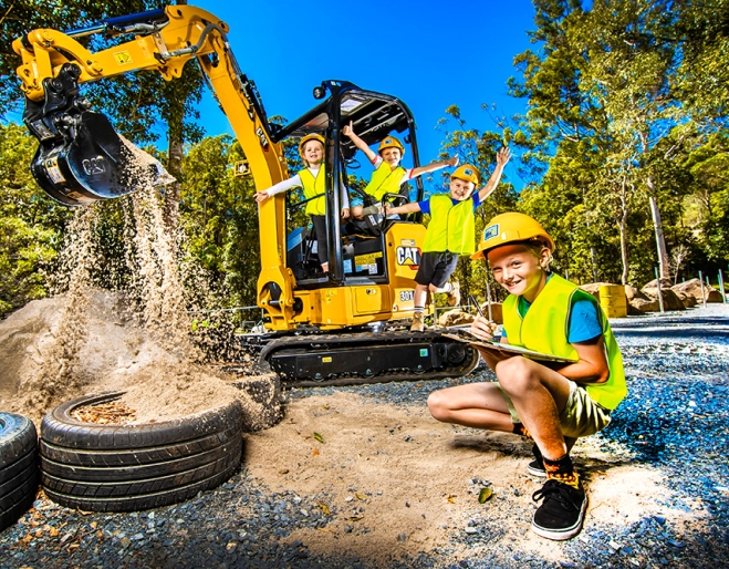 Child squatting down with clipboard and three children playing on a mini excavator digging sand at Dig IT Tamborine Mountain