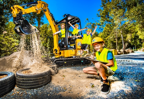 Child squatting down with clipboard and three children playing on a mini excavator digging sand at Dig IT Tamborine Mountain