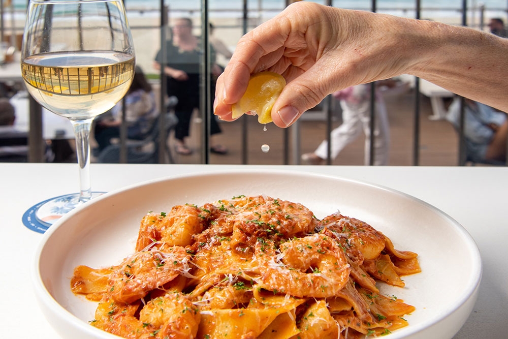 Hand squeezing lemon on dish of pasta