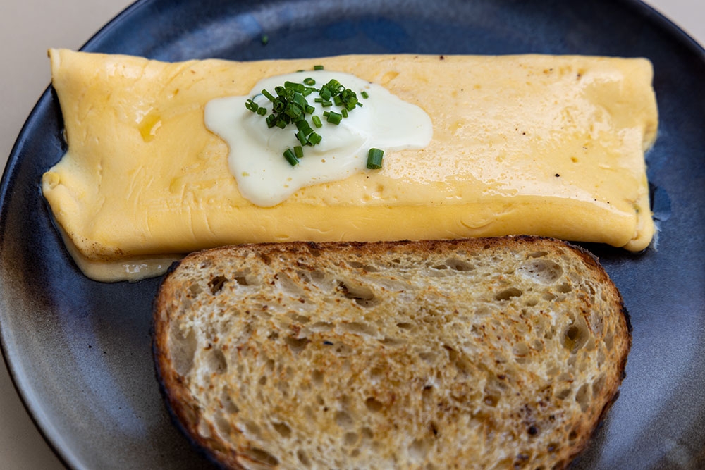 European-Style Folded Eggs with nutty gouda, crème fraîche and chives served on toasted sourdough on a plate