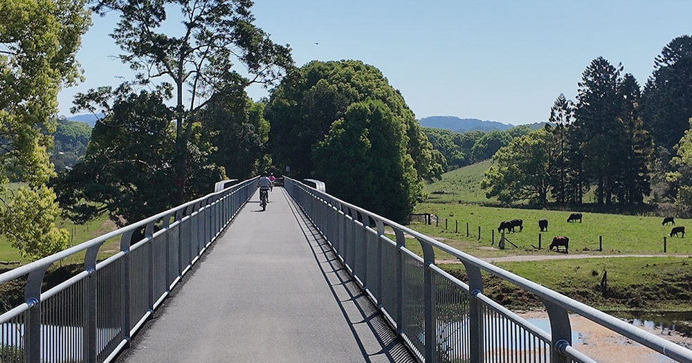 Cyclist on e-bike crossing rail bridge overlooking lush countryside